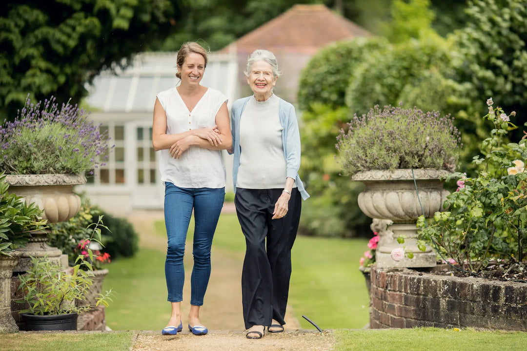 Live-in Care Client and her Carer walking in garden with plants and conservatory in background