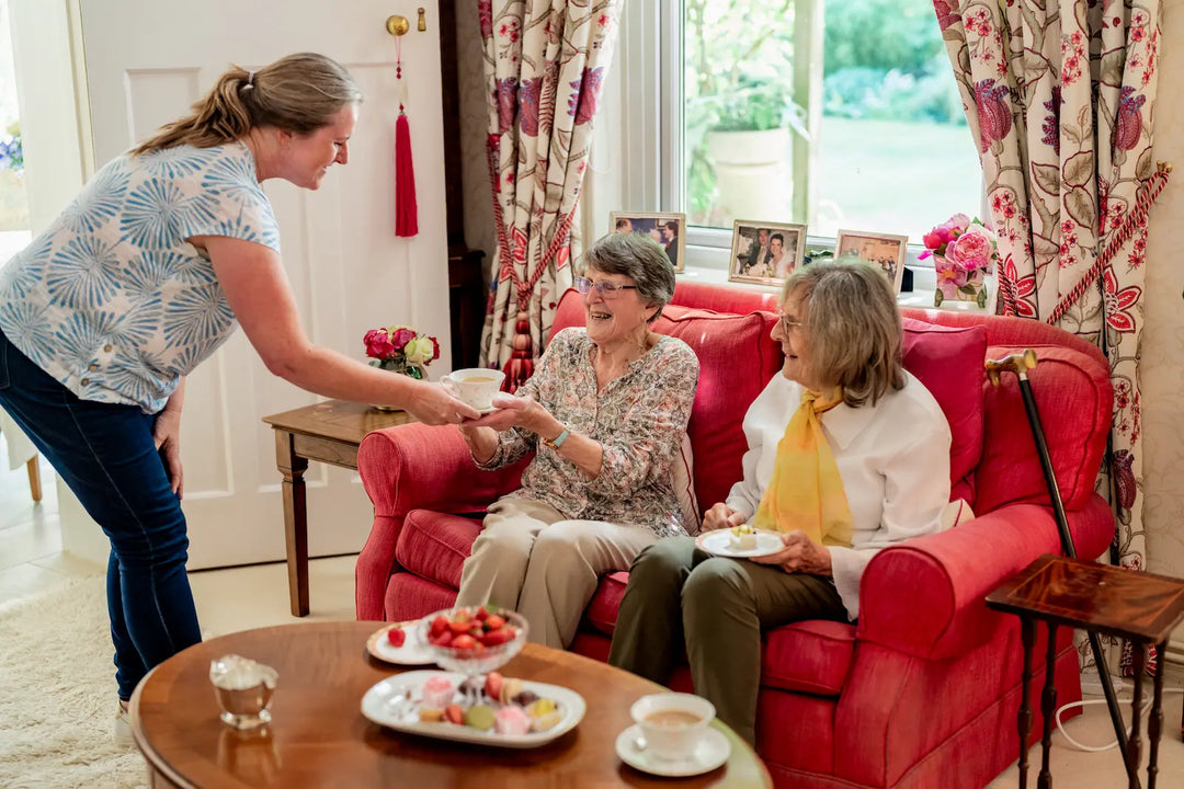 Carer serving tea to elderly woman at home, showing live-in care in a familiar home environment