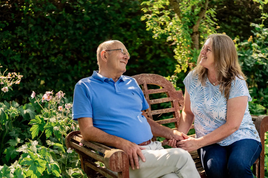 Carer and male client sat on bench in garden talking