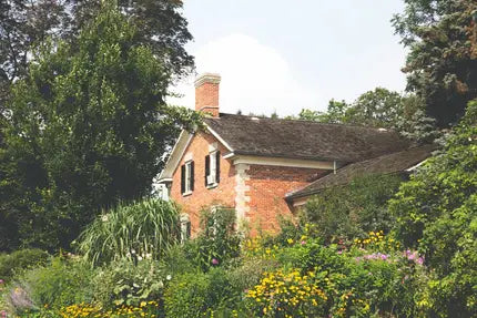 Brick house with a garden in front, surrounded by trees and greenery
