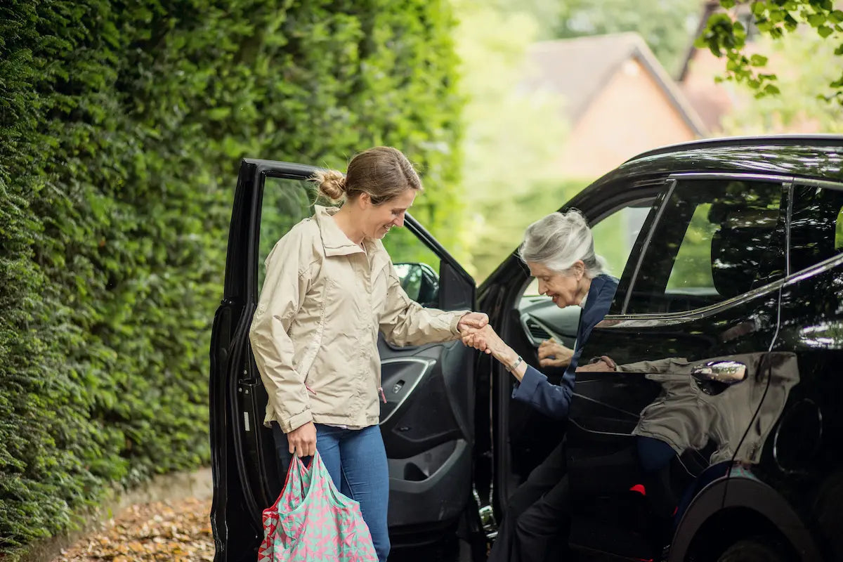 Carer helping an elderly woman step out of a car during a day out, illustrating live-in care support at home in the UK.