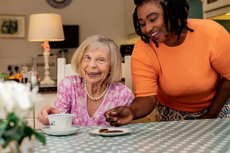 Elderly lady with her live-in carer sharing tea and laughing