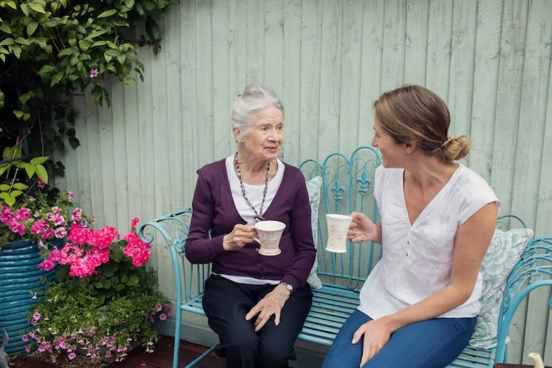 Two women sitting on a garden bench, drinking tea and talking.