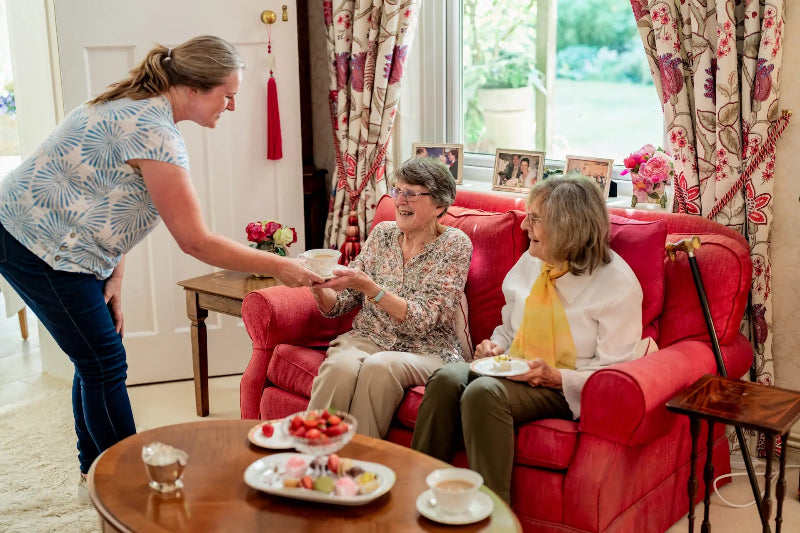 Live-in carer serving tea to two elderly ladies at home